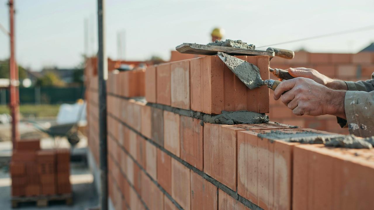 Mason applying fresh mortar to a brick end before placing it into the wall.