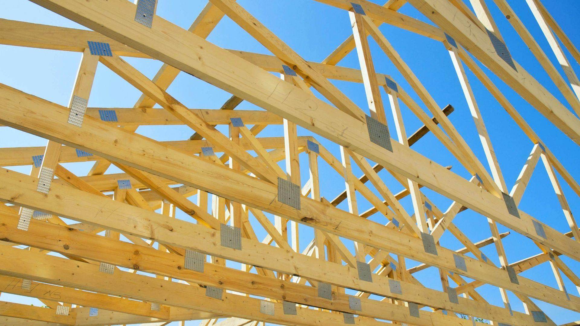 Wooden roof trusses framing under bright blue sky at residential construction site