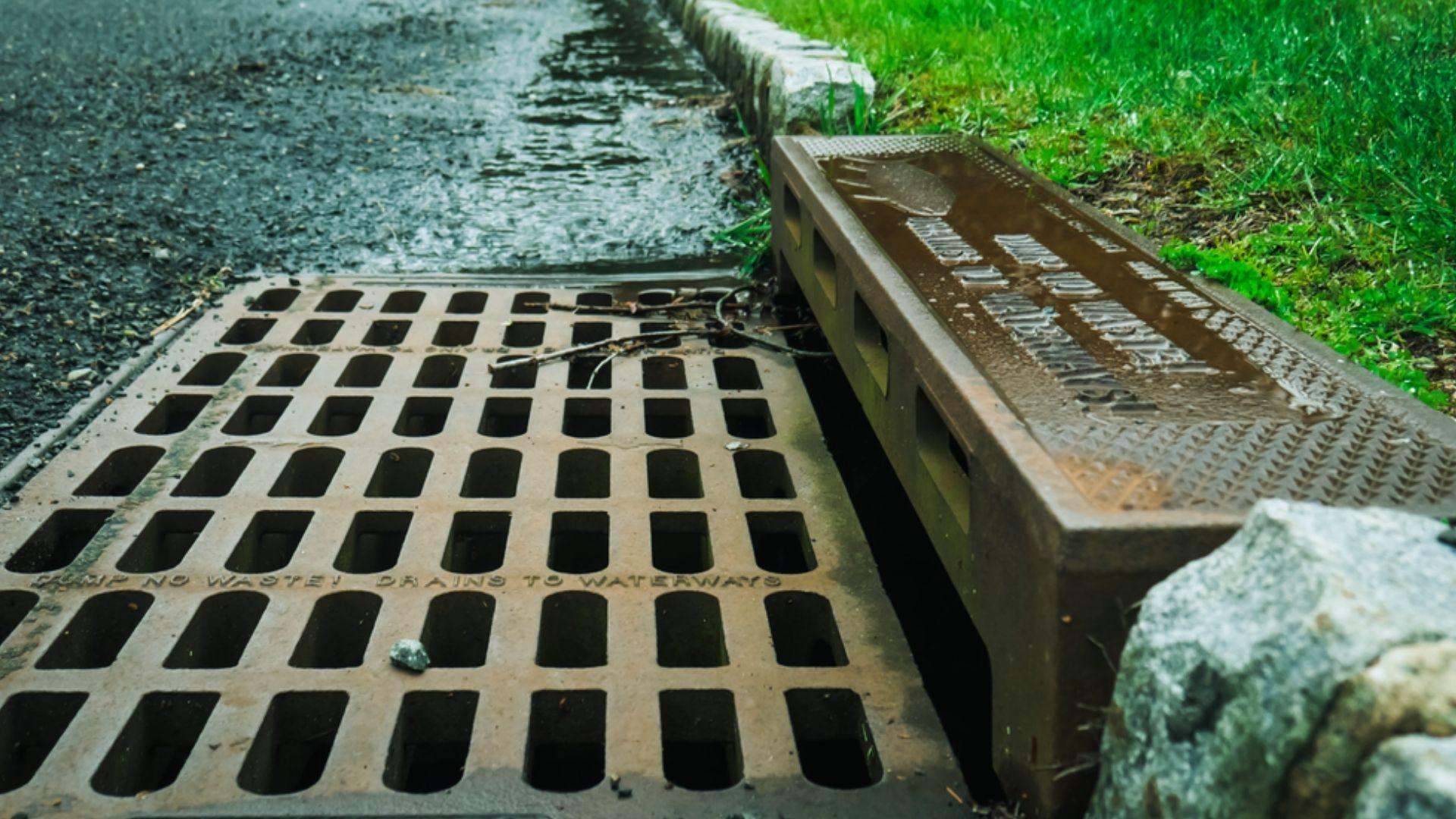 Rainwater flowing into rusted storm drain grate on street curb with grass