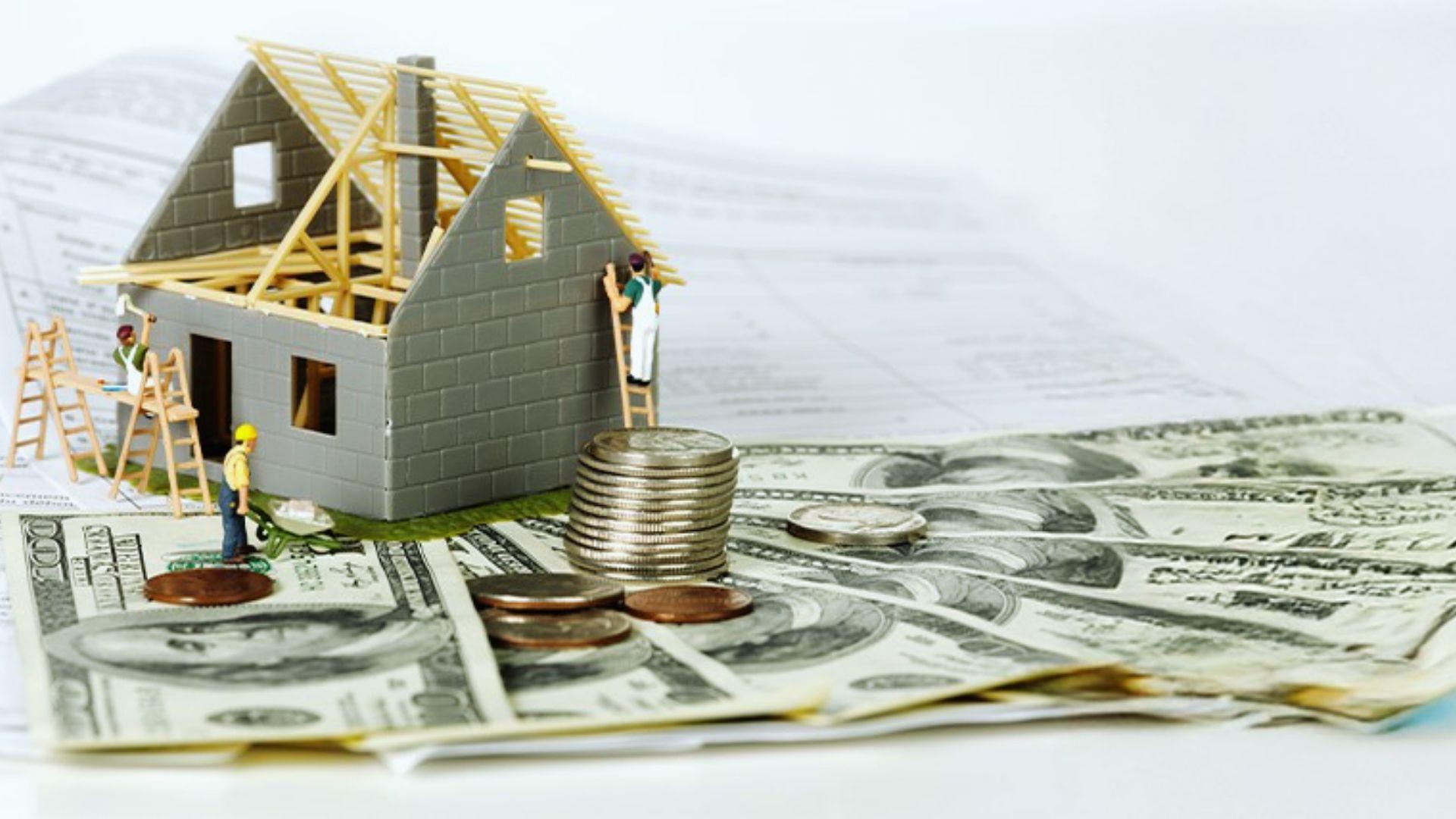 Miniature house under construction on US dollars with coins and blueprints