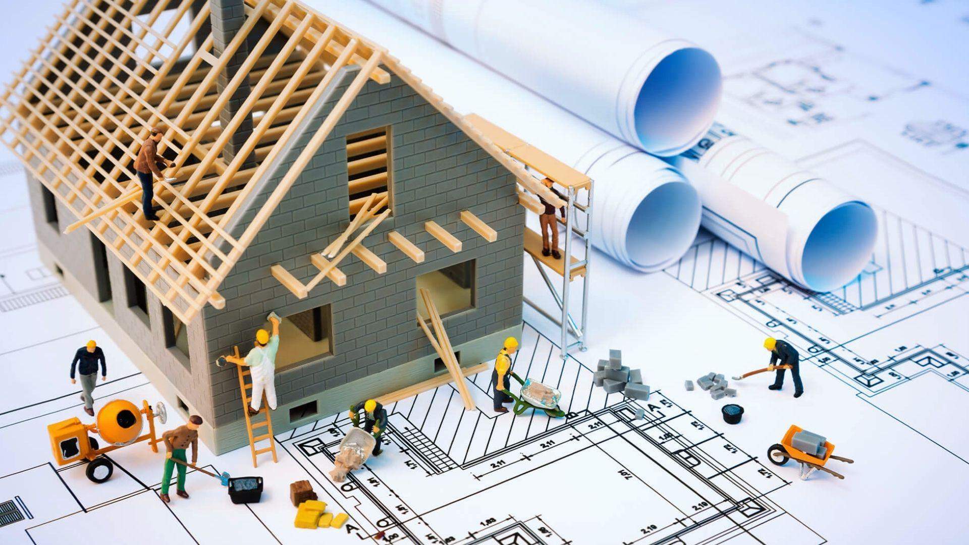 Miniature construction workers building model house on architectural blueprints for residential project