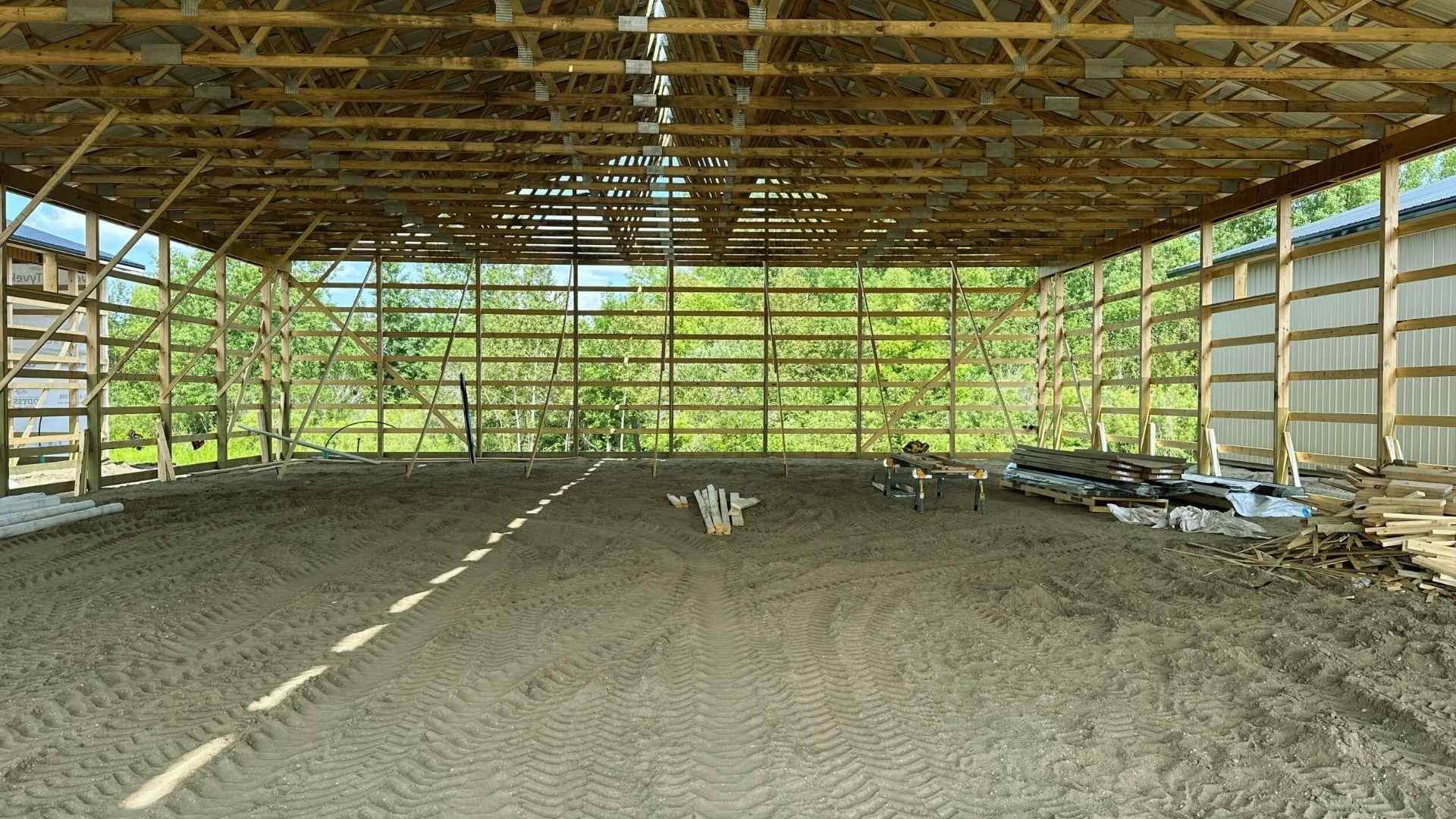 Interior wooden pole barn frame with roof trusses and dirt floor during construction
