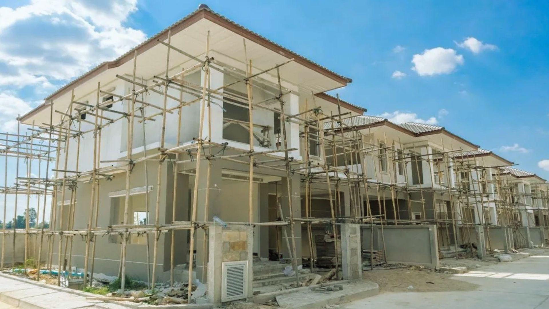 Row of two-story houses under construction with bamboo scaffolding on sunny day