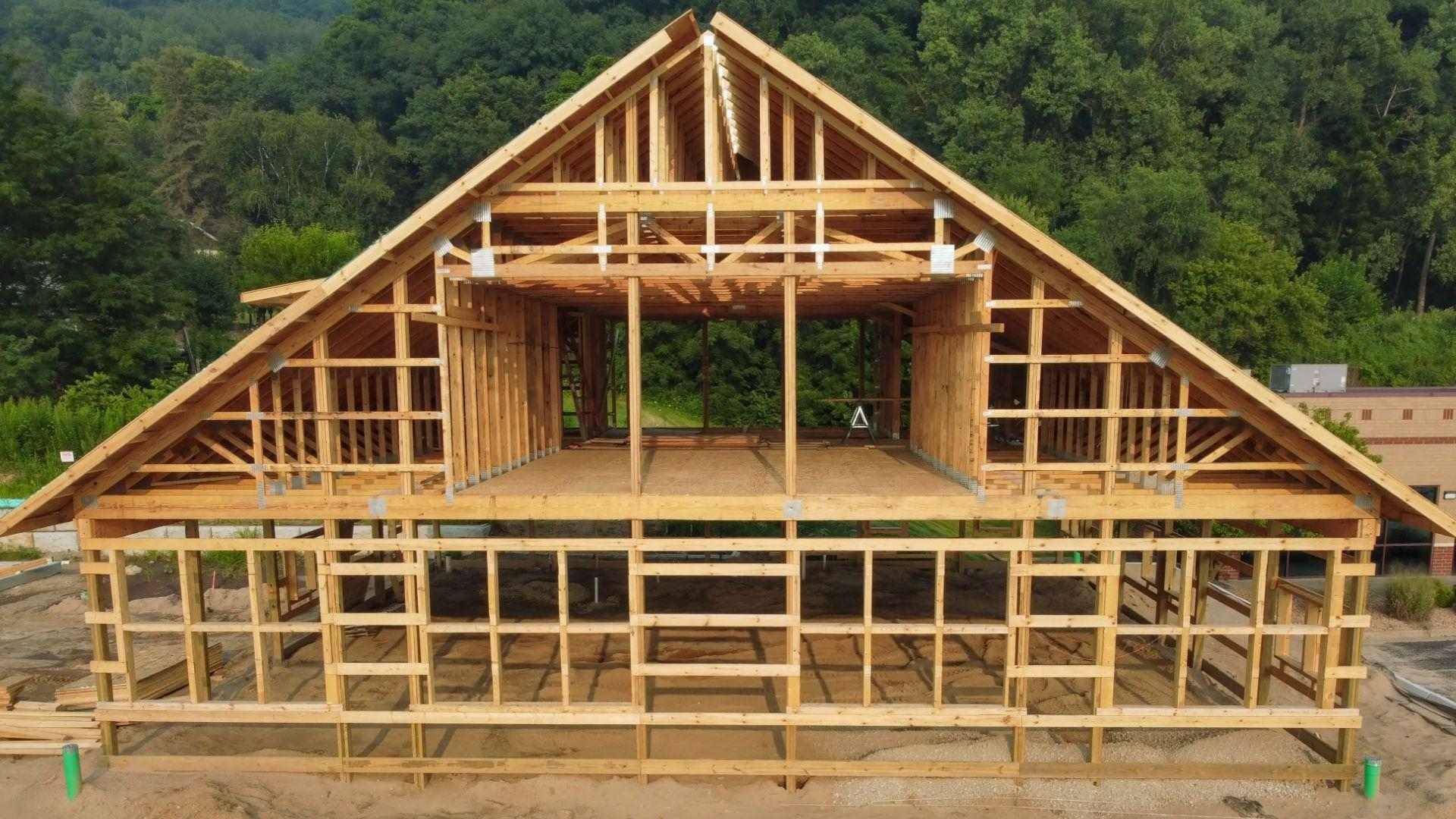 Two-story wooden house frame construction with gable roof trusses on dirt building site