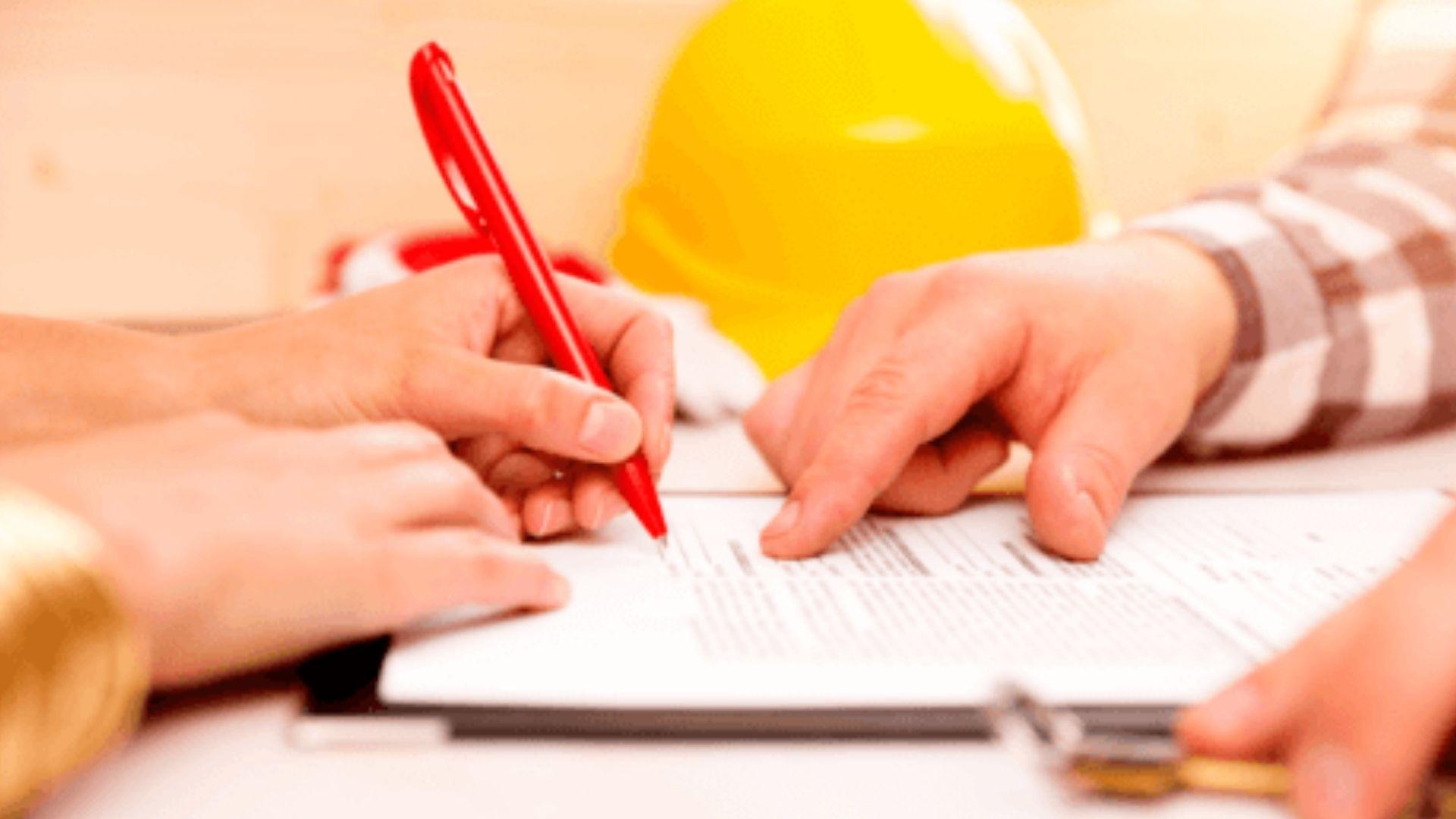 Contractor and client signing construction agreement with red pen and hard hat