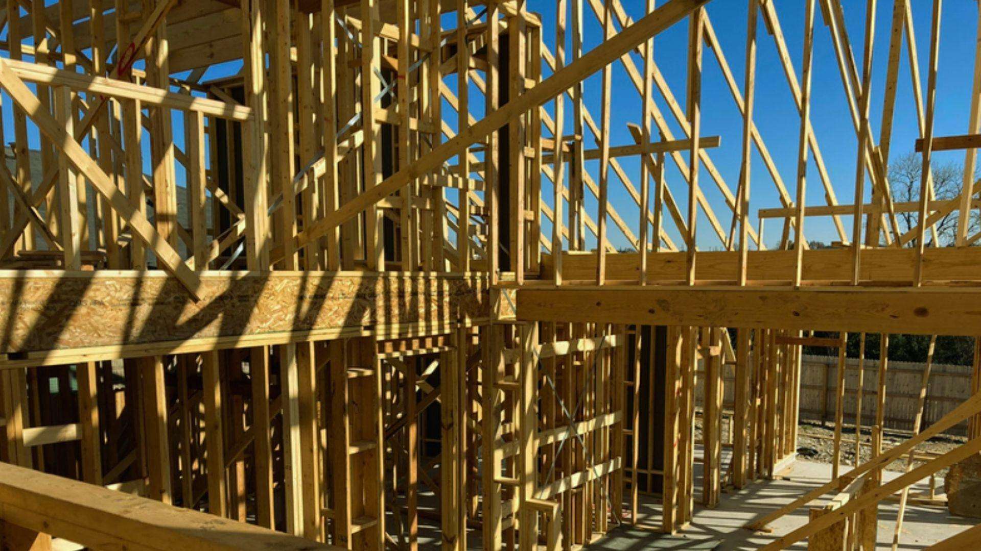 Interior wooden house framing with lumber wall studs and roof trusses under blue sky