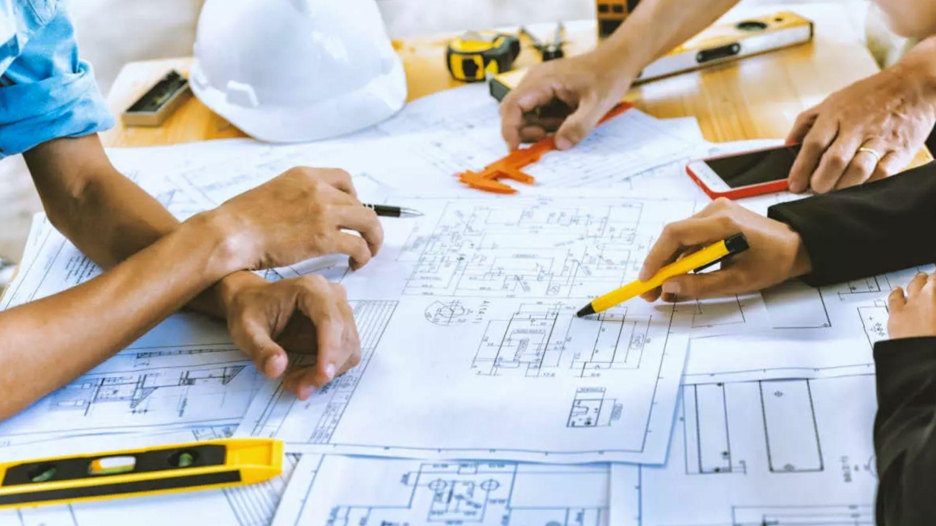 Construction team reviewing architectural blueprints with hard hat and measuring tools