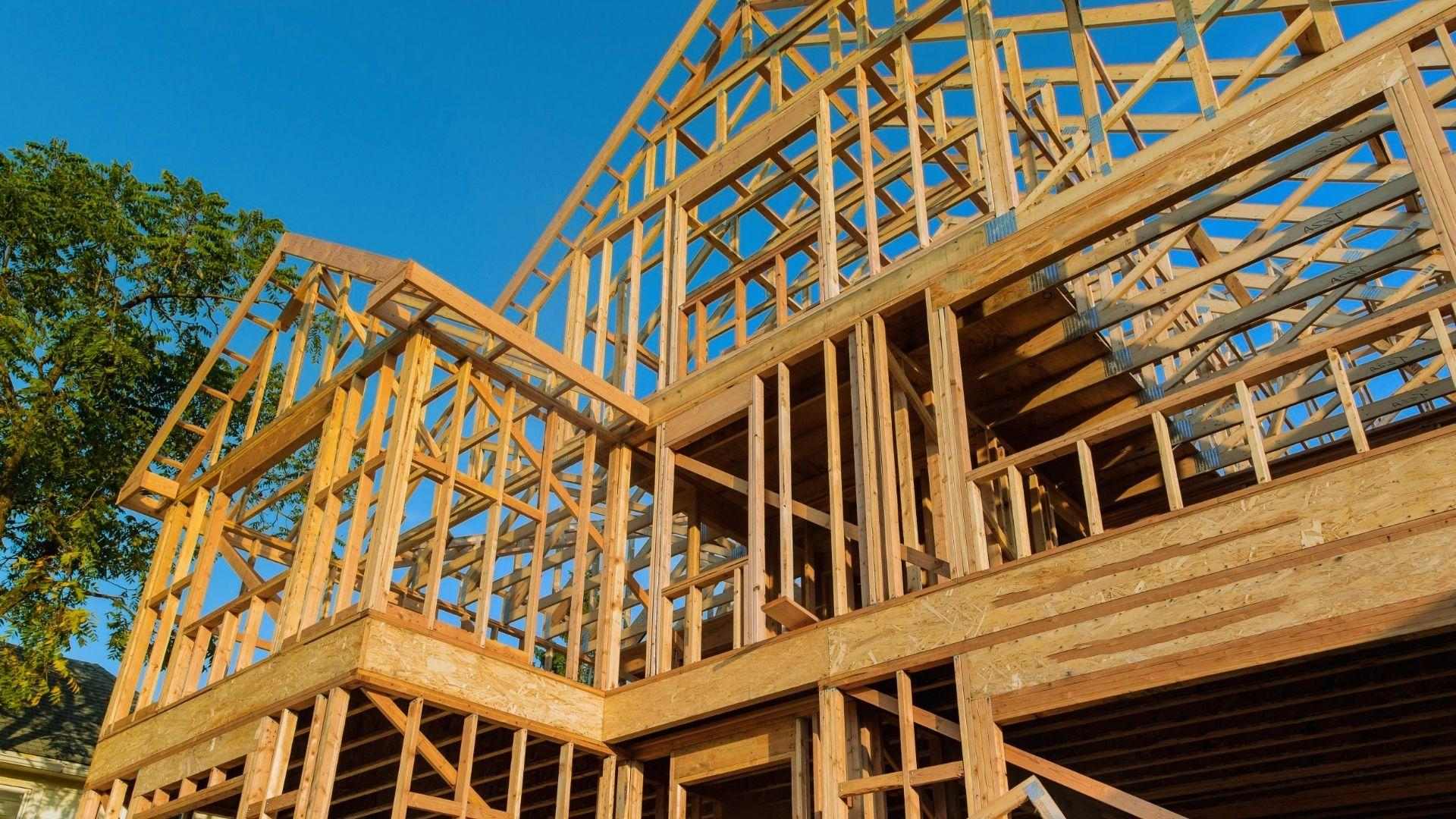 Two story house wood framing construction with lumber beams under bright blue sky