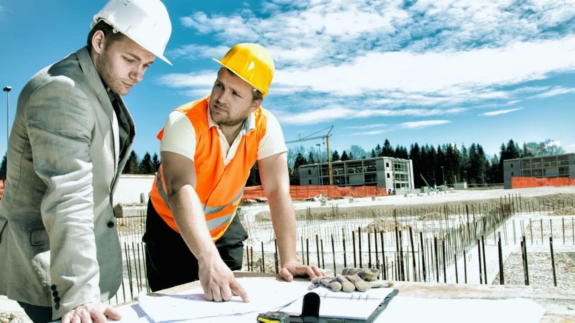 Engineer and manager reviewing blueprints at building foundation construction site