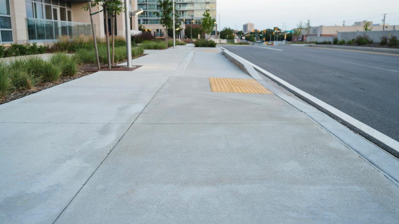 Empty concrete sidewalk with yellow tactile paving beside road at dusk near modern building.