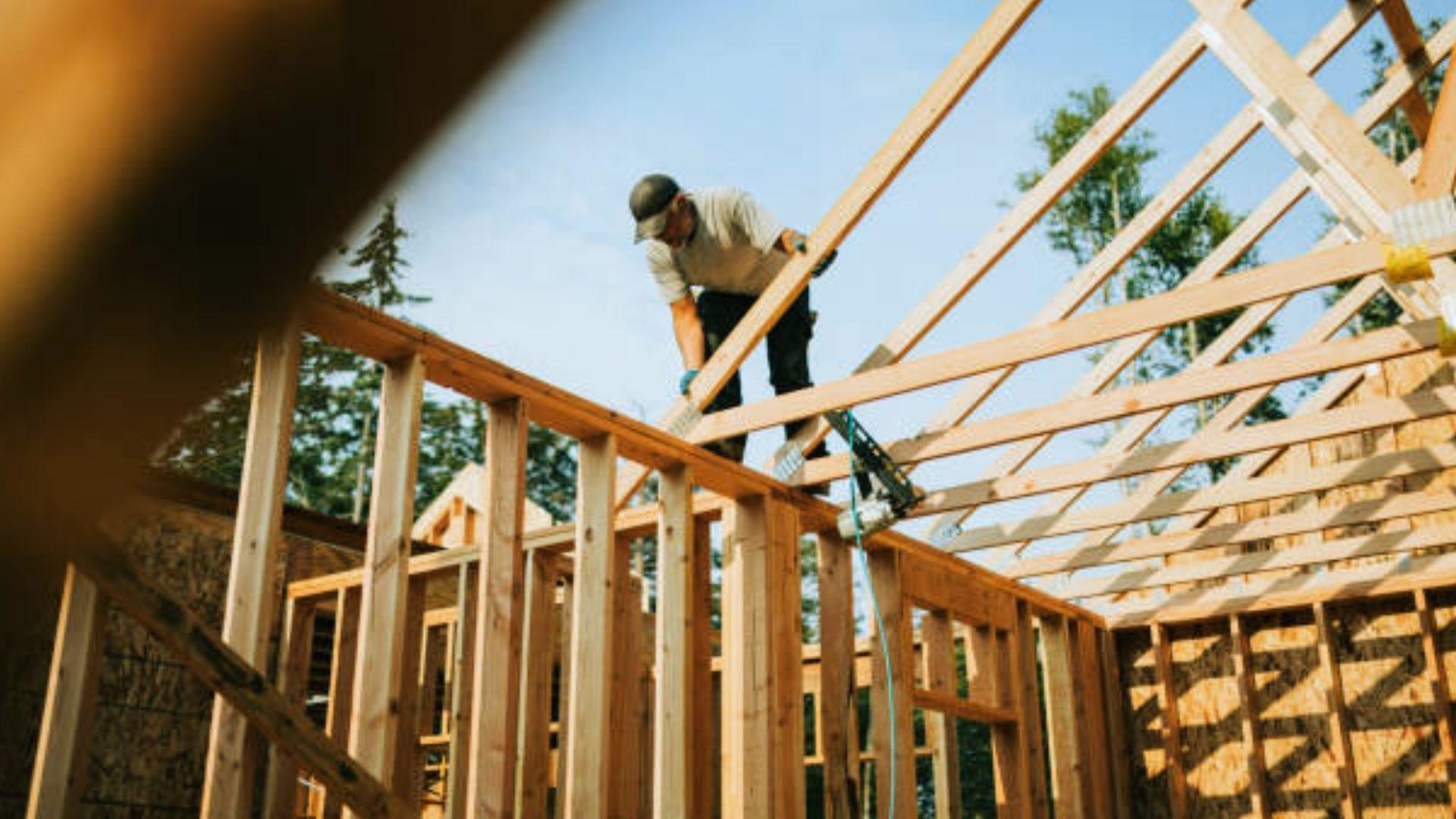 Carpenter installing wooden roof trusses on house frame during residential construction