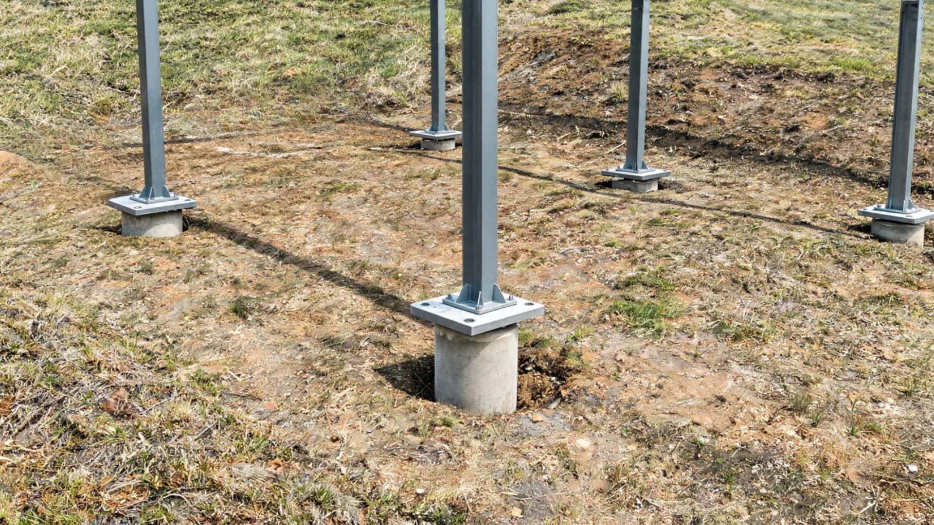 Carport posts stand on concrete piers embedded in uneven ground along a sloped residential site.
