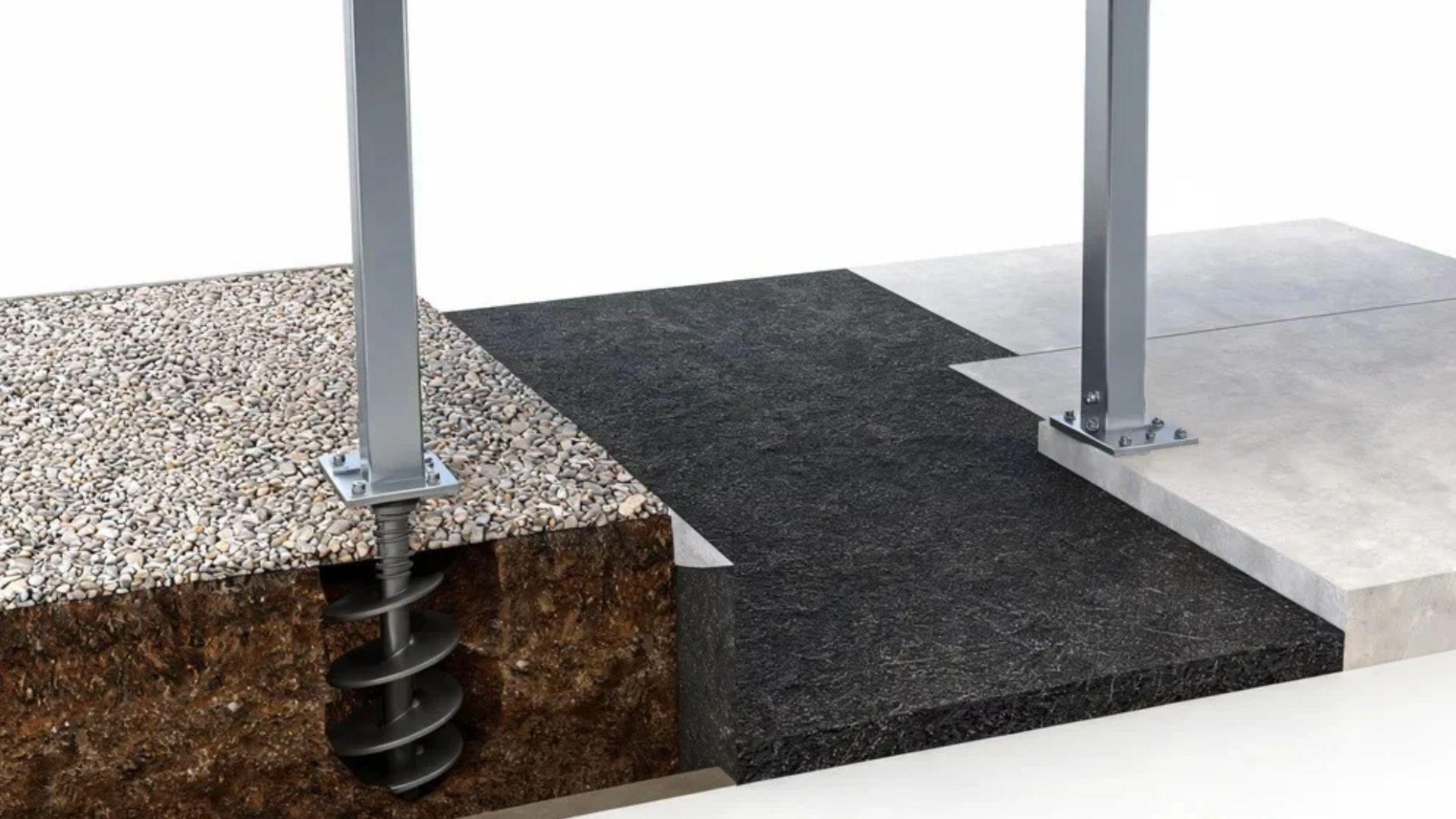 Ground anchor secures a carport post beside gravel, asphalt, and an existing concrete driveway slab.