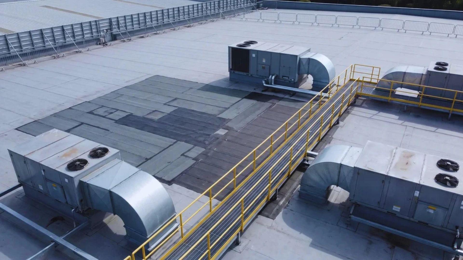 Commercial rooftop with HVAC equipment, access walkway, safety barriers, and a membrane repair area.