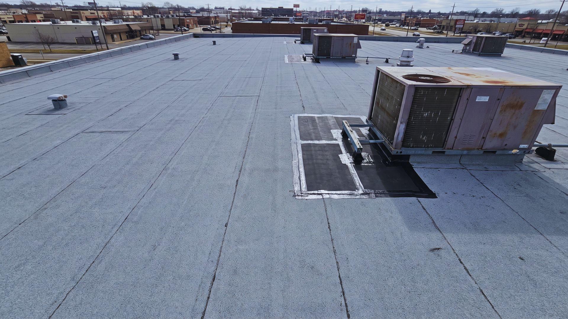 Commercial flat roof with membrane seams, rooftop HVAC units, and a localized repair area.