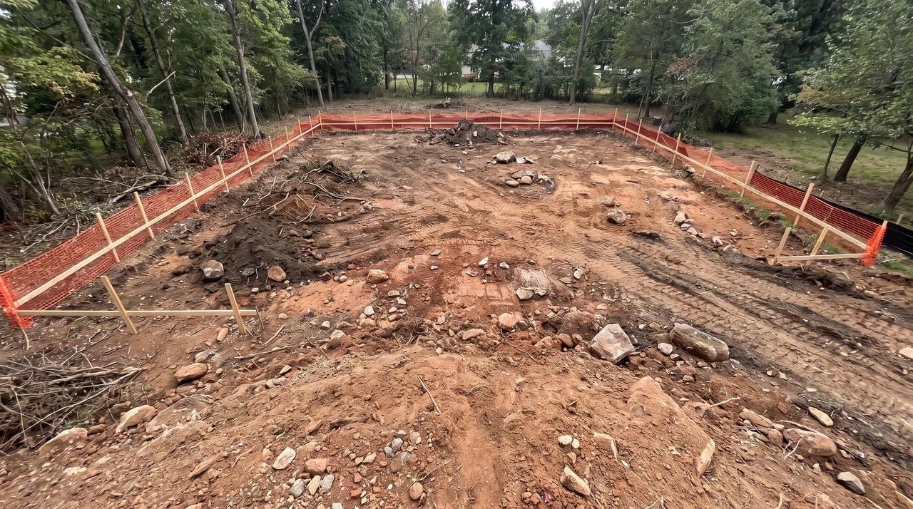 Exposed construction footprint with stripped topsoil, rocks, and cleared debris.