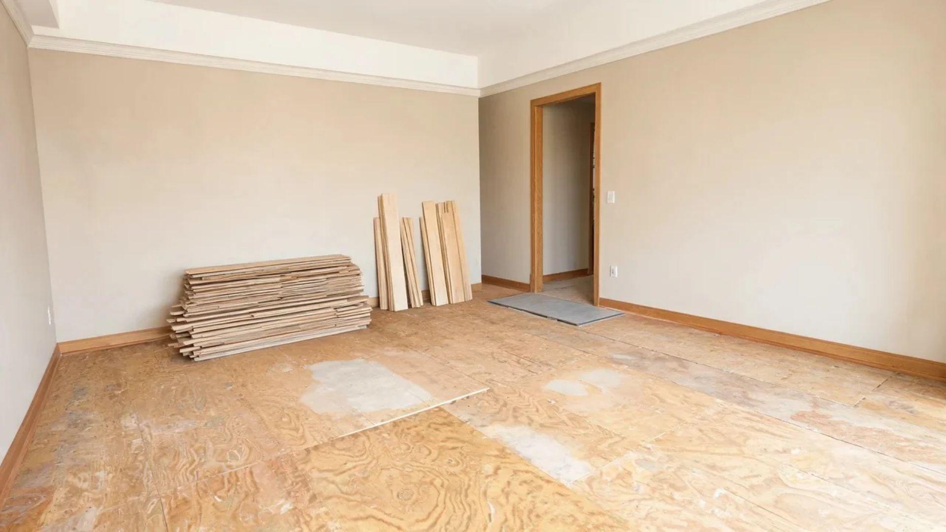 Removed flooring, subfloor patching materials, baseboard trim, and a transition strip in a renovation room.File name: hidden-vinyl-flooring-installation-costs