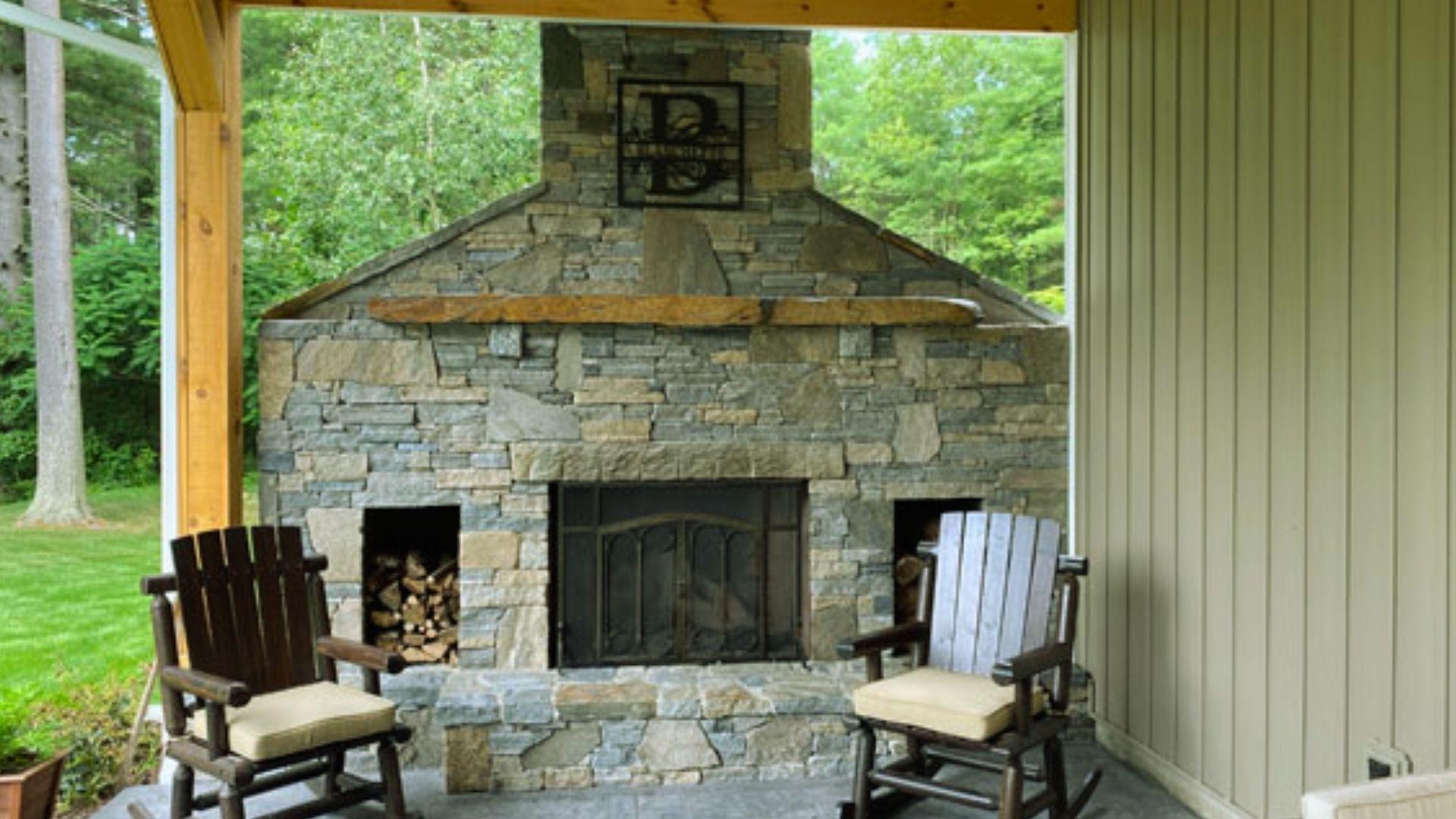 Outdoor stone fireplace with wooden mantel and rocking chairs on covered patio