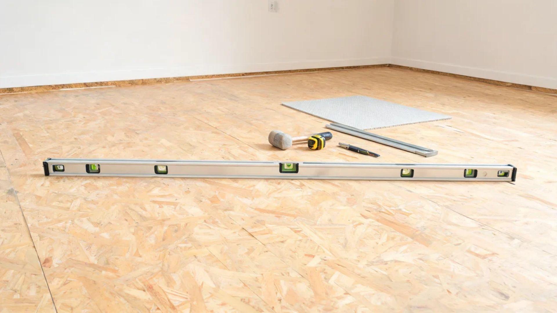 Long level and flooring tools arranged on a cleared subfloor before vinyl plank installation. File name: vinyl-floor-subfloor-preparation