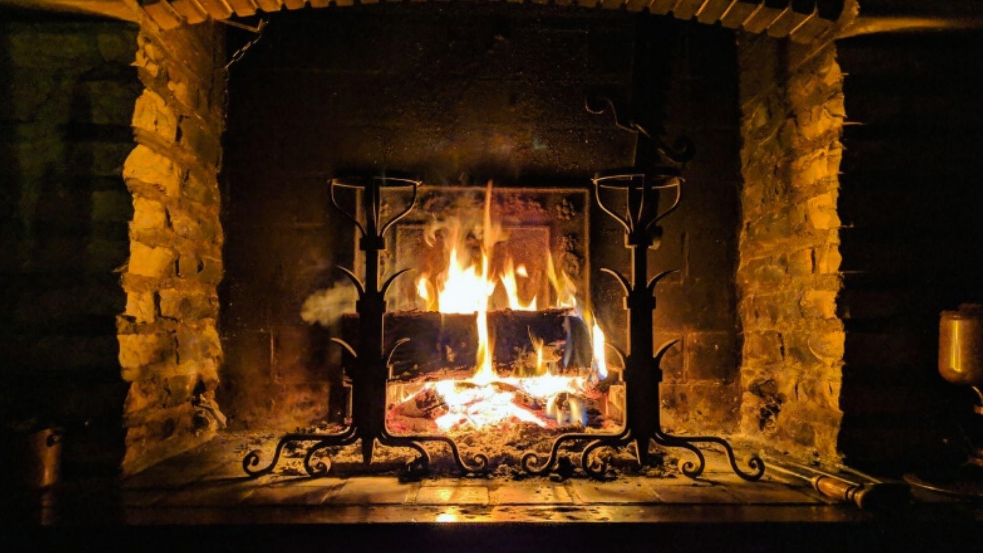 Cozy brick fireplace with roaring fire burning between ornate iron andirons at night creating warm ambiance