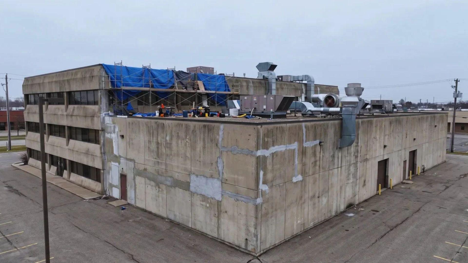 Commercial building with rooftop equipment and visible exterior concrete repair work.File name:commercial-building-repair-cost