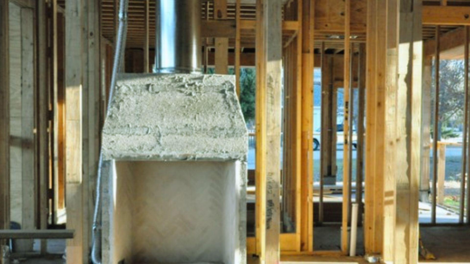 Unfinished concrete fireplace with metal chimney pipe surrounded by wooden wall framing at construction site