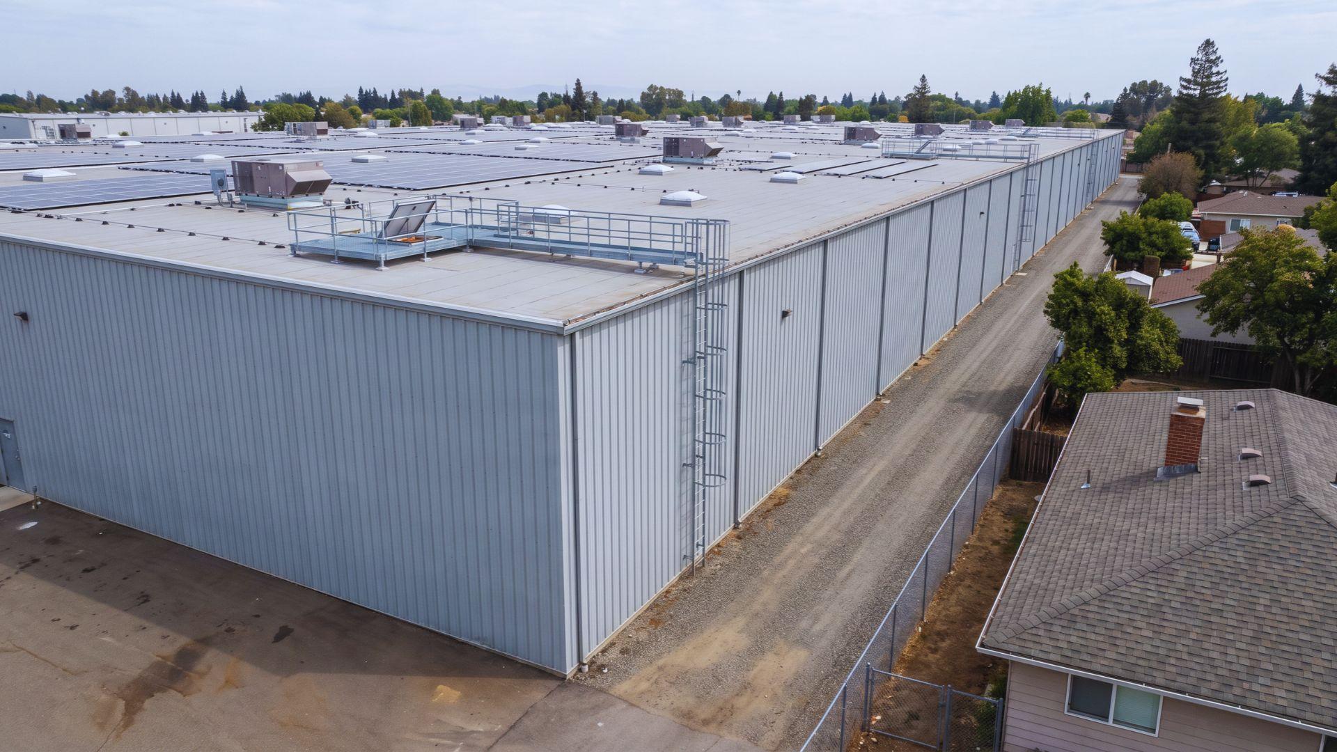Large commercial warehouse with rooftop equipment beside a smaller residential house.File name: commercial-residential-repair-costs