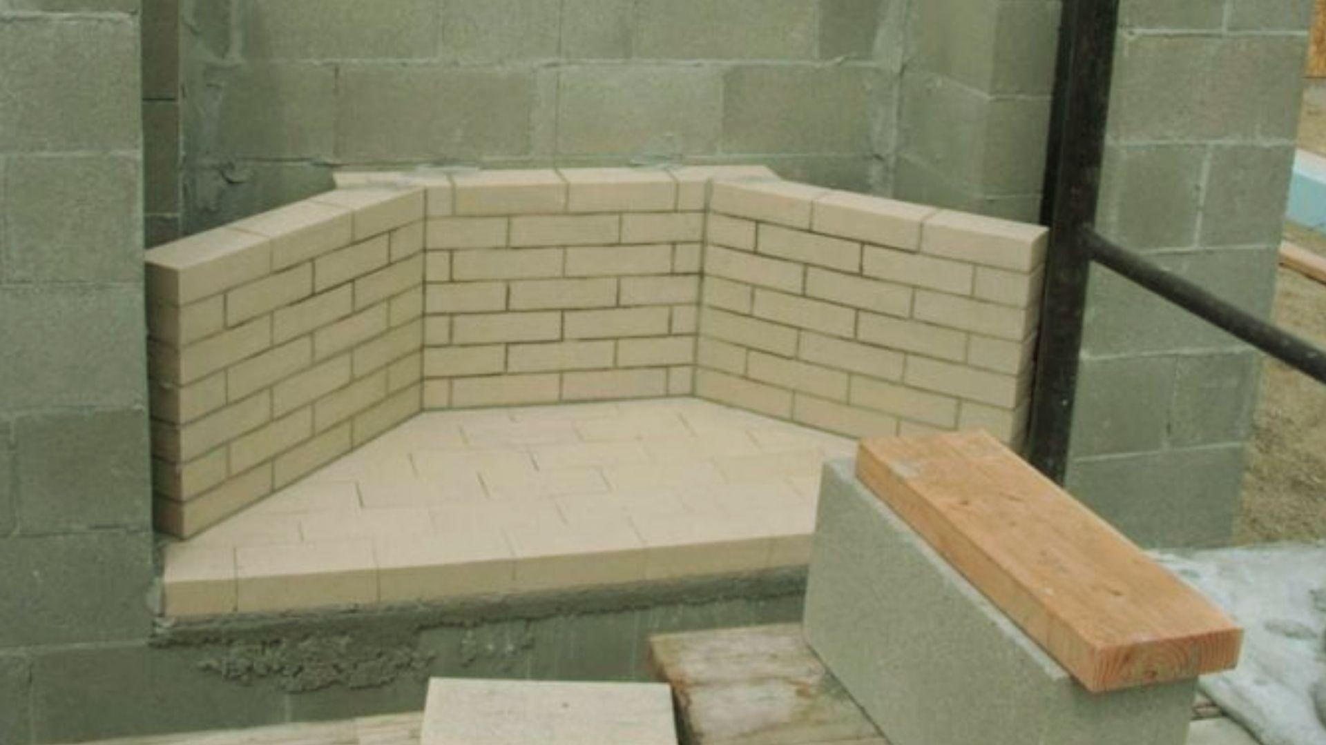 Fireplace under construction with beige firebrick hearth surrounded by gray concrete block walls on scaffolding