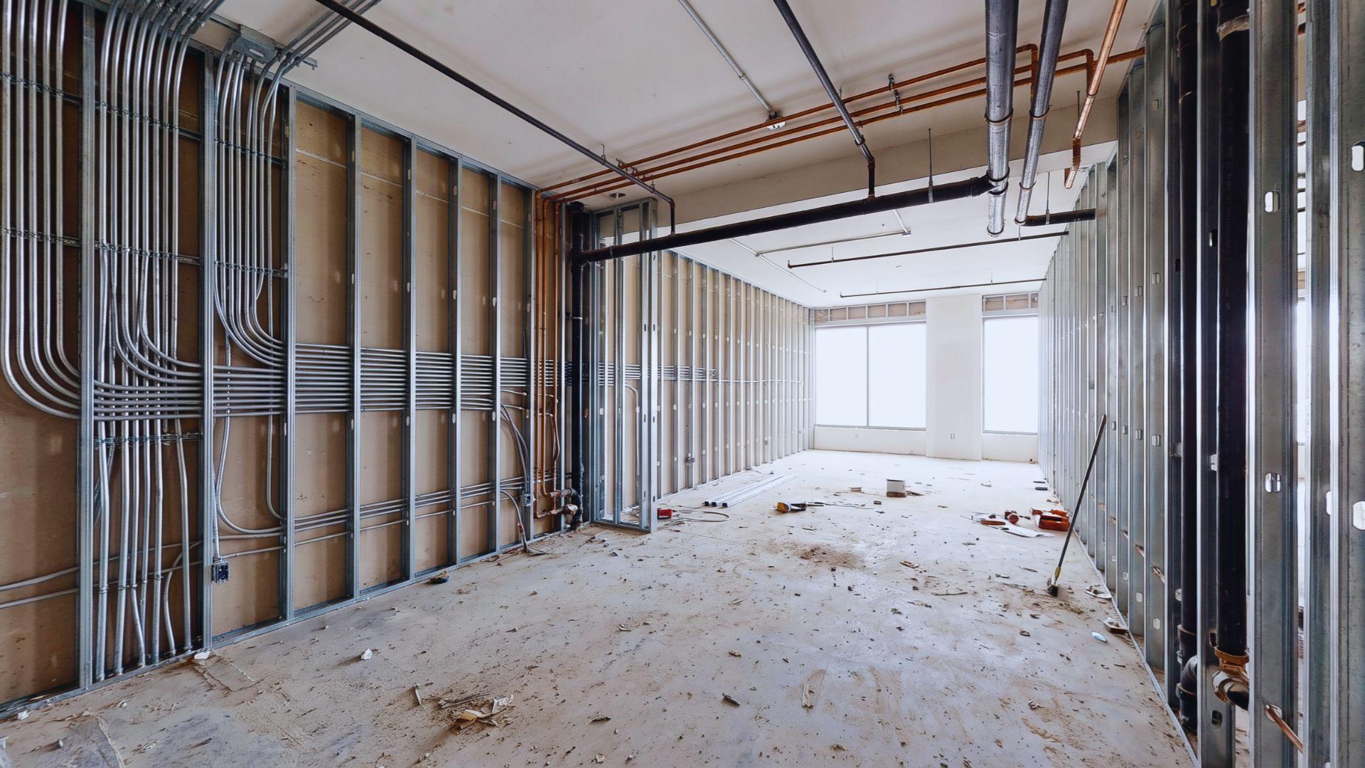 Commercial interior with exposed framing, pipes, electrical conduits, and unfinished flooring during renovation.File name: commercial-building-renovation