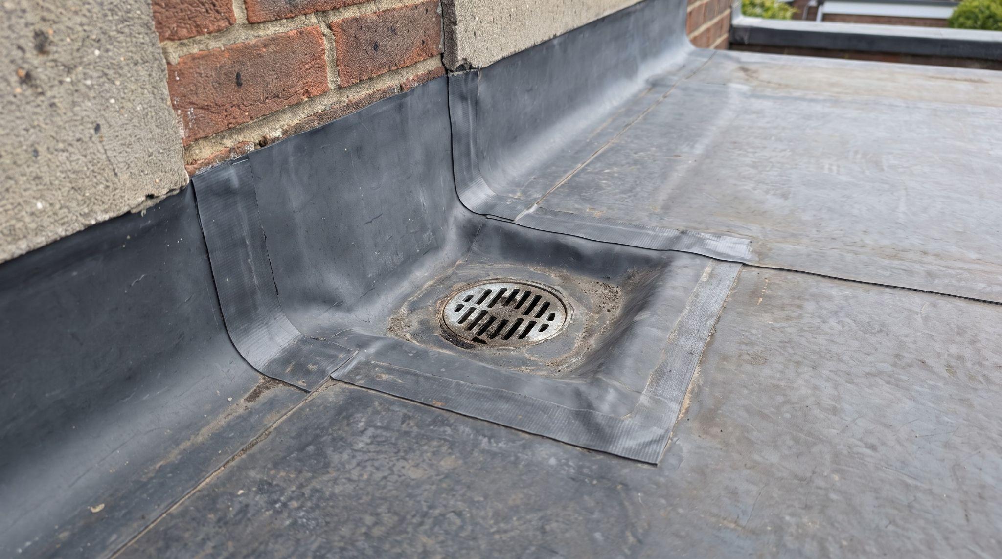 Flat roof flashing bonded at a wall junction with a drainage outlet at the lowest point.