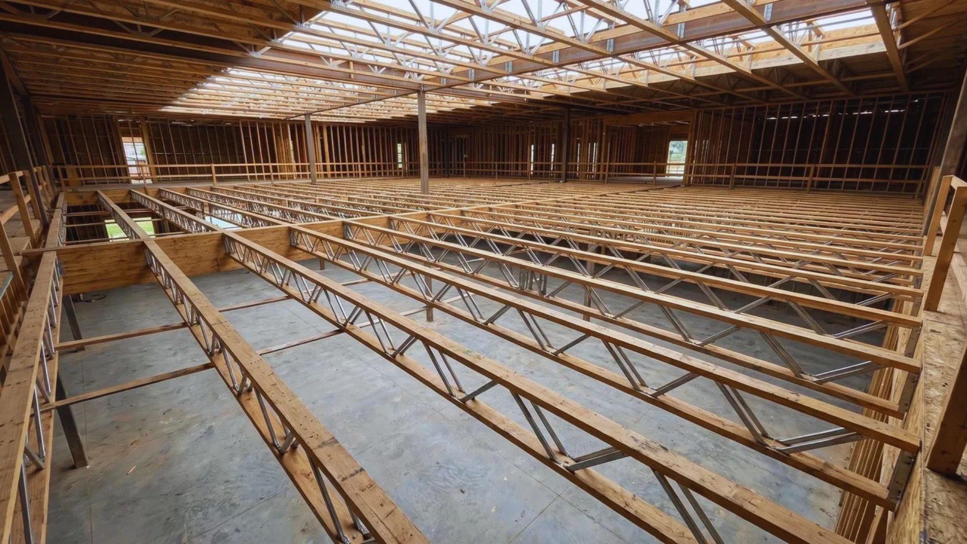 Open-web floor trusses span an unfinished interior with a wide open space beneath them.