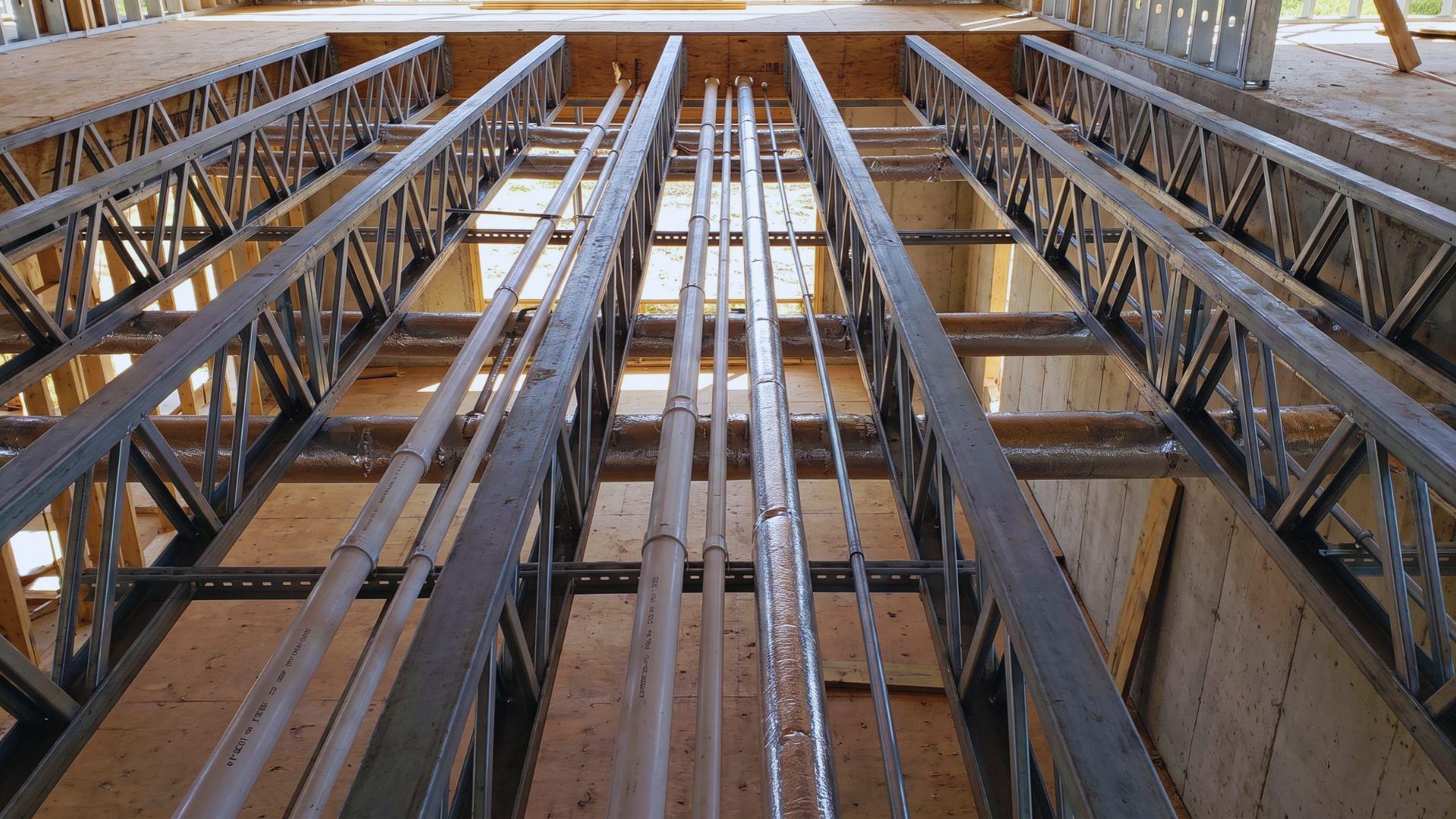 Pipes and ducts pass through open spaces between the web members of floor trusses.