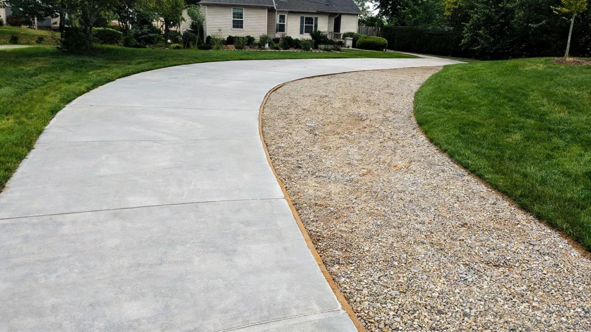 Curved concrete driveway beside an exposed compacted aggregate base on a residential property.