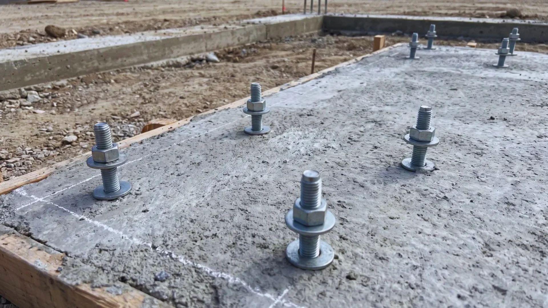 Anchor bolts protruding from a concrete slab at the planned steel column positions.