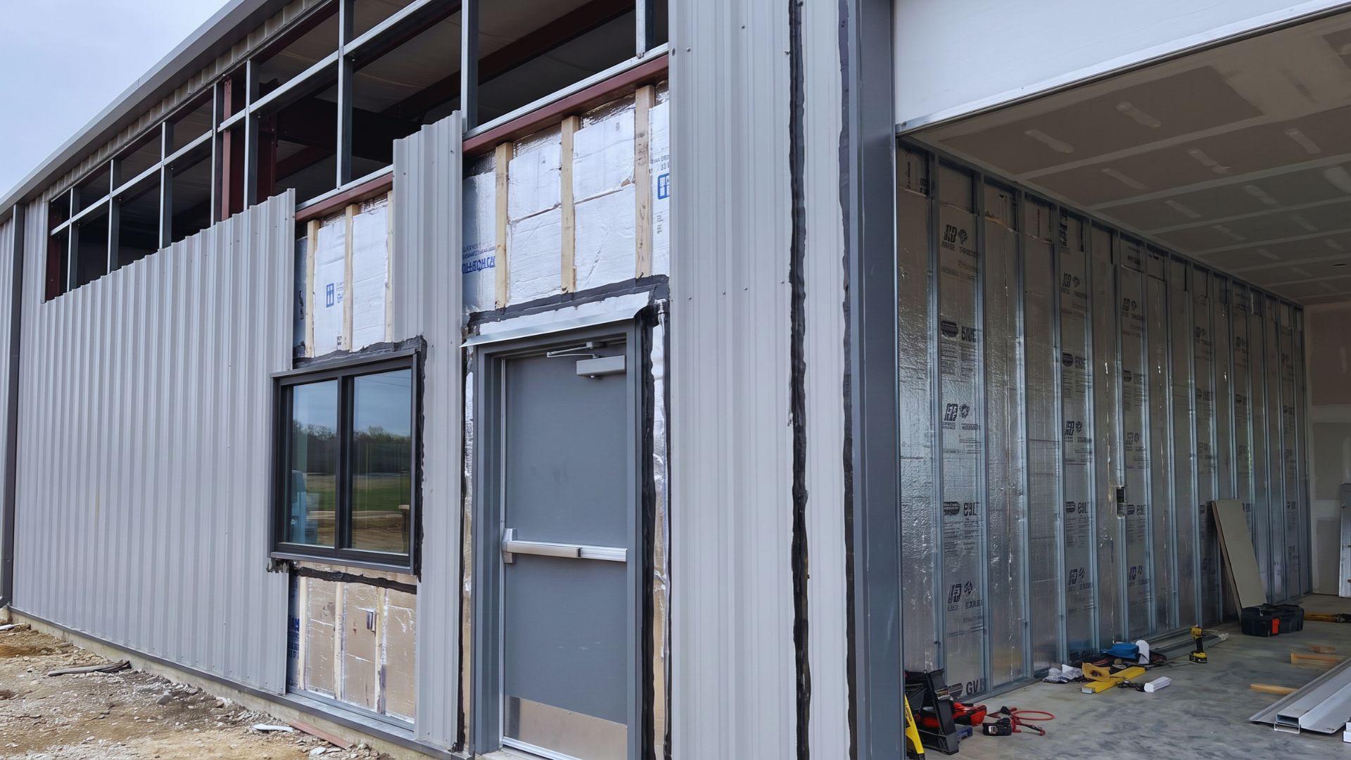 Insulation fitted behind metal wall panels beside an installed window and walk door.