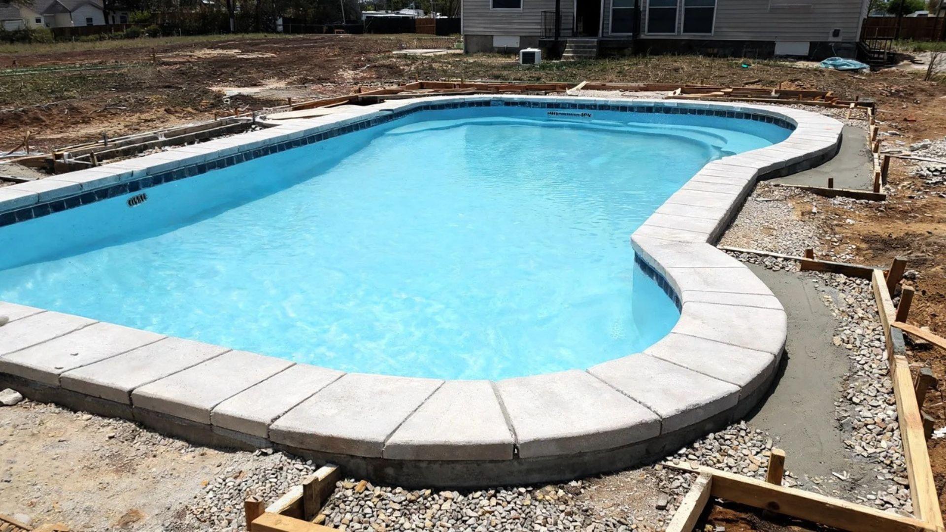 Inground pool with finished interior surface, level coping, and surrounding deck under construction.