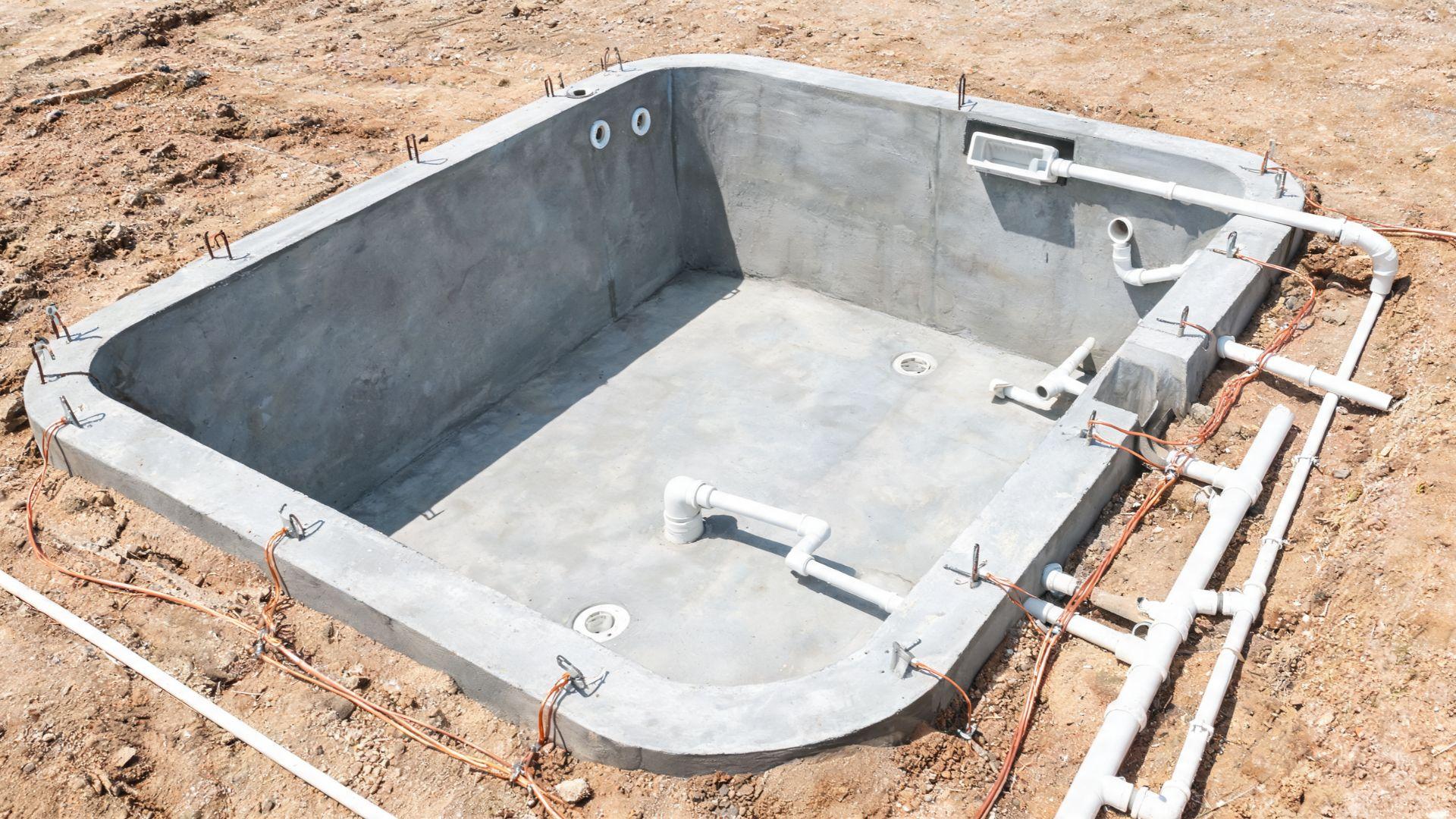 Pool plumbing rough-ins and electrical bonding connections exposed before backfill and deck work.