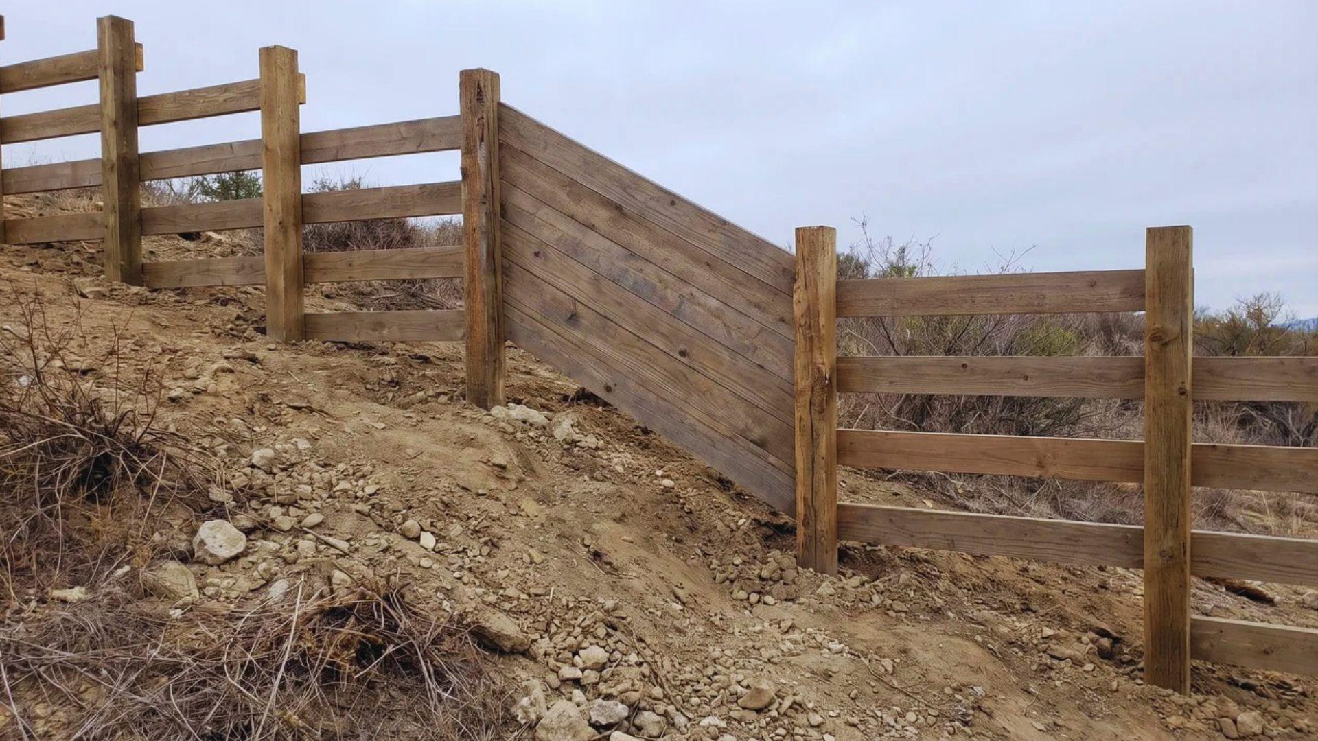 Angled fence panels follow the slope beside level panels arranged in steps along the same hill.