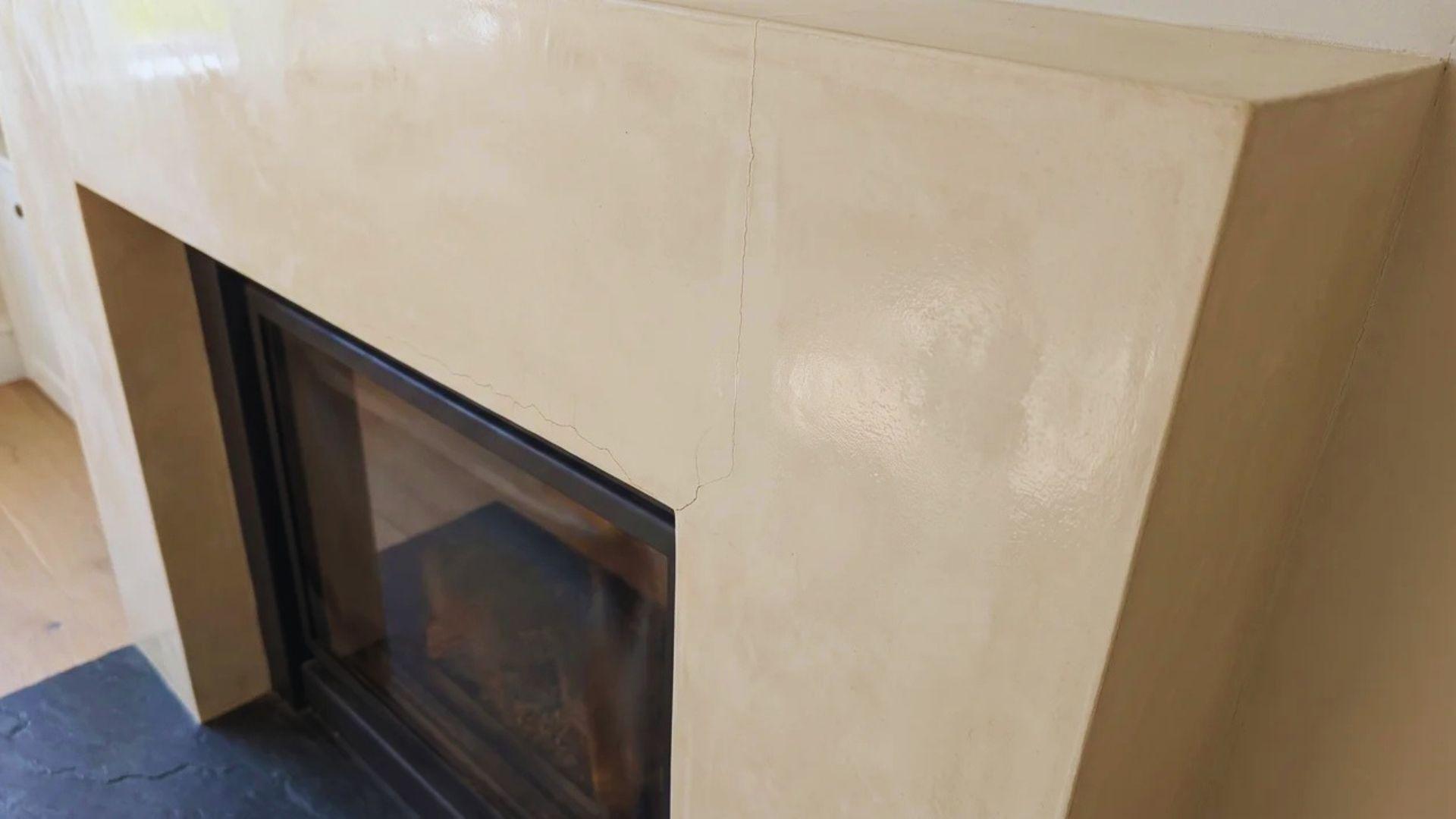 Hairline cracks and uneven sheen on a Venetian plaster fireplace surround near the firebox.