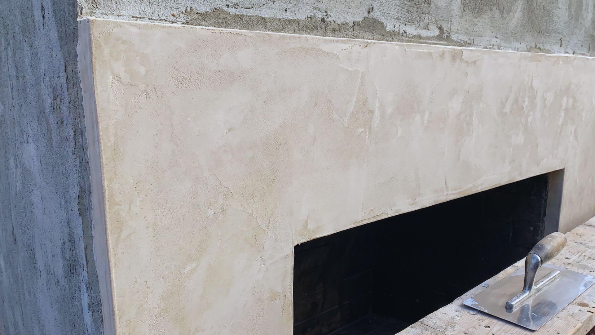 Thin Venetian plaster finish covers a leveled brick fireplace surround beside a flexible trowel.